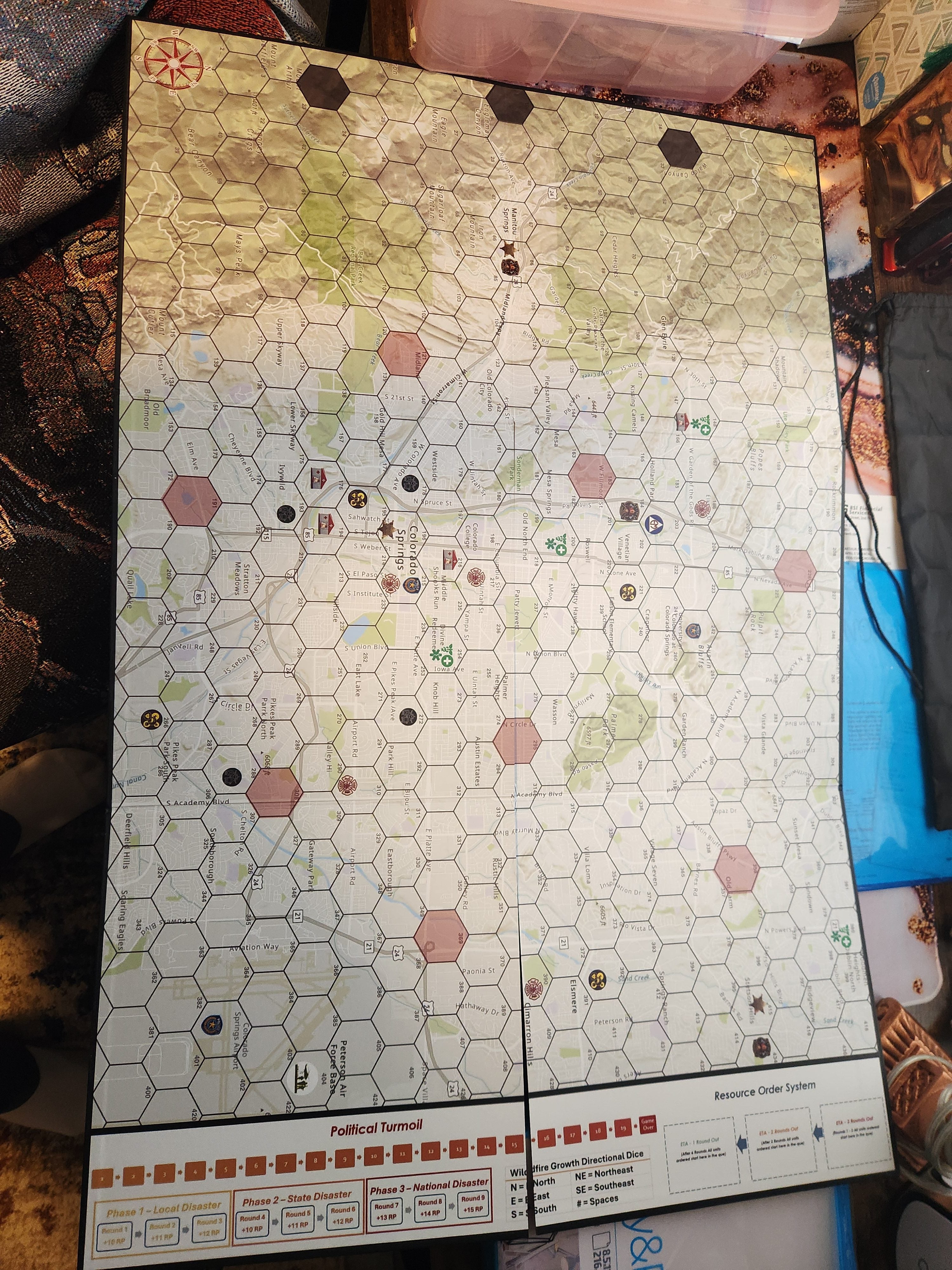 Top-down view of the Wildfire Mayhem game board showing a hex-grid map with icons and terrain details
